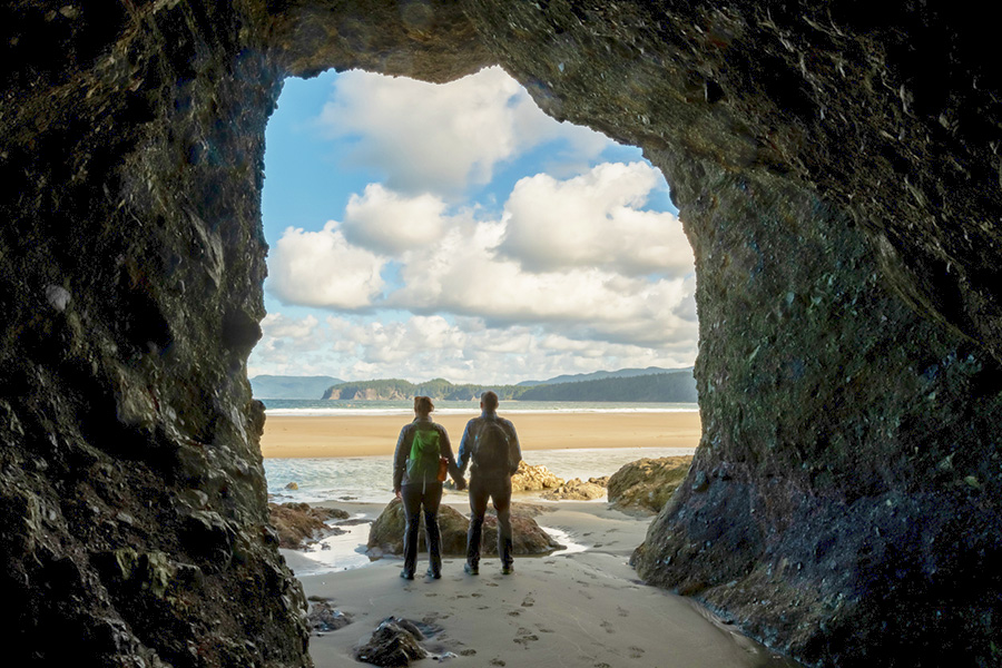 Hiker Couple Hold Hands In Sea Cave